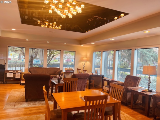 dining space with plenty of natural light, recessed lighting, a raised ceiling, and light wood-type flooring