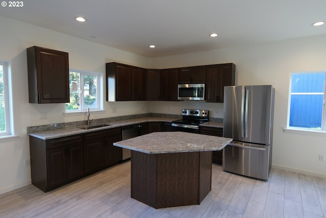 kitchen featuring light stone counters, dark brown cabinetry, a sink, appliances with stainless steel finishes, and a center island