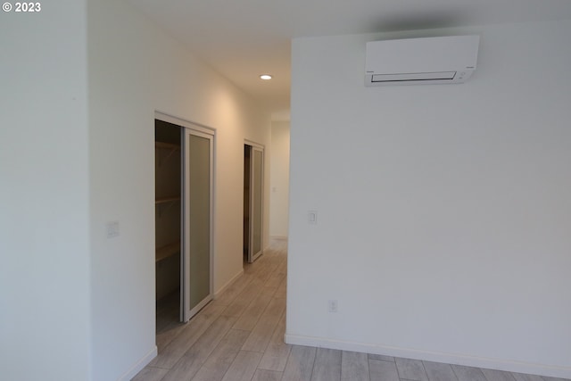 hallway with baseboards, light wood finished floors, a wall unit AC, and recessed lighting