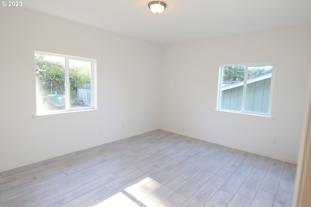 empty room featuring baseboards, a healthy amount of sunlight, and light wood finished floors