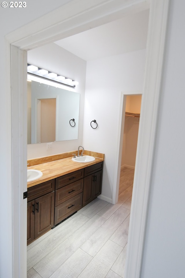 full bath with double vanity, a sink, a walk in closet, and baseboards