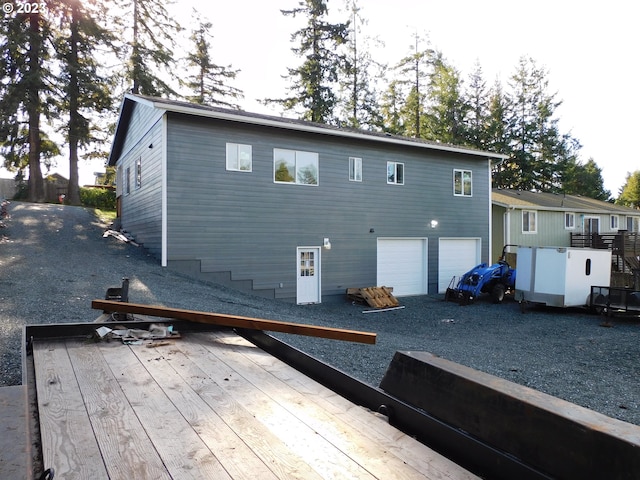 rear view of property featuring driveway, an attached garage, and a wooden deck