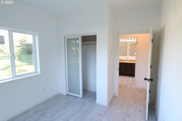 unfurnished bedroom with light wood-style flooring, a closet, baseboards, and a sink