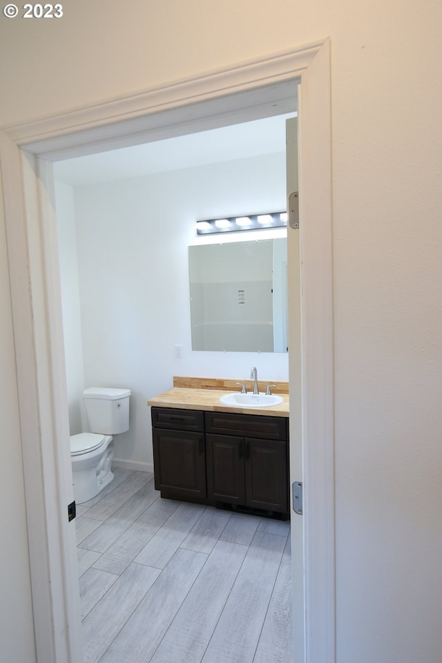 bathroom with wood finished floors, vanity, toilet, and baseboards