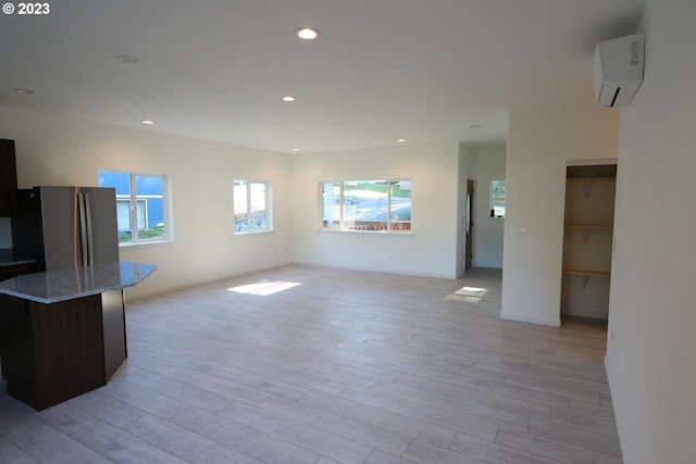 unfurnished living room featuring a wall unit AC, a healthy amount of sunlight, light wood-style floors, and recessed lighting