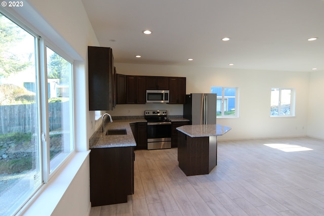 kitchen featuring appliances with stainless steel finishes, a center island, a sink, and light stone counters