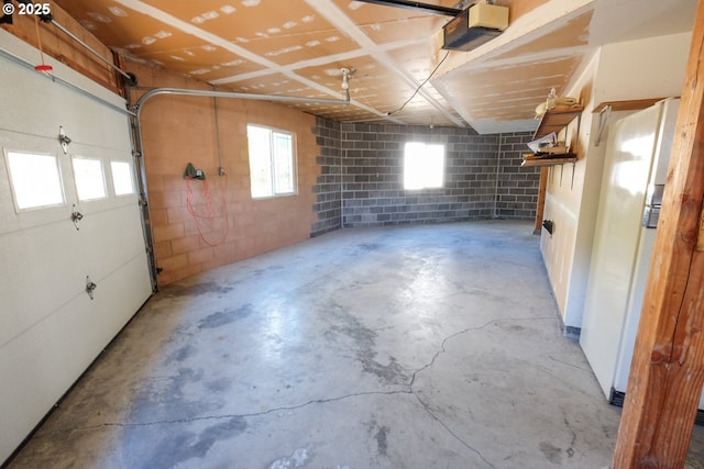garage featuring concrete block wall, a garage door opener, and freestanding refrigerator