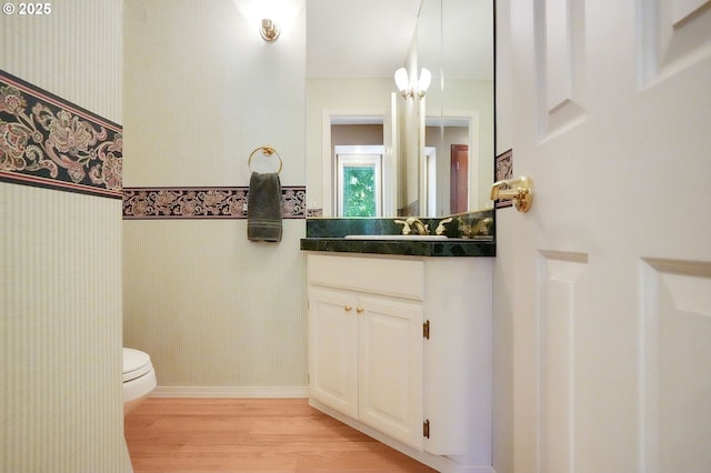 bathroom featuring wallpapered walls, baseboards, toilet, wood finished floors, and vanity