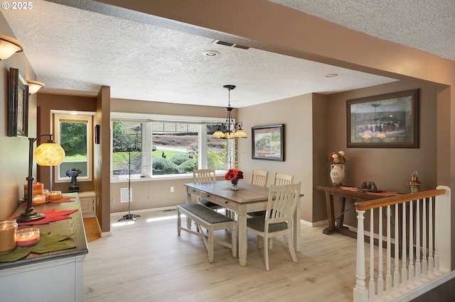 dining room with a textured ceiling, a notable chandelier, visible vents, baseboards, and light wood finished floors