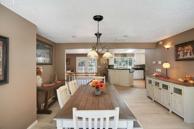 dining area with a textured ceiling, visible vents, light wood-style flooring, and baseboards