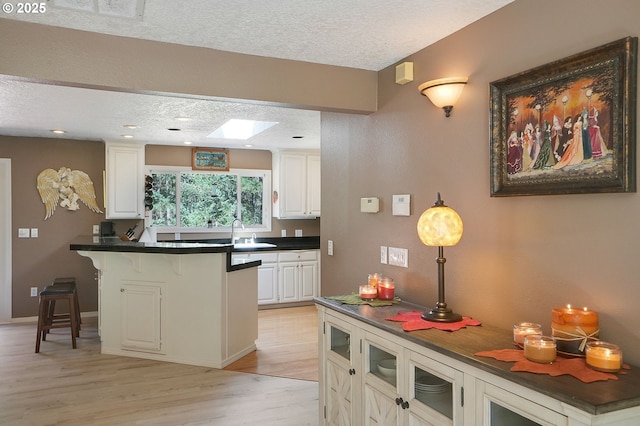 kitchen featuring a textured ceiling, a breakfast bar, dark countertops, and a sink