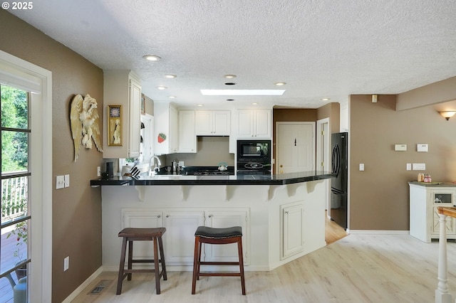 kitchen with visible vents, light wood-style floors, black appliances, a peninsula, and a kitchen breakfast bar