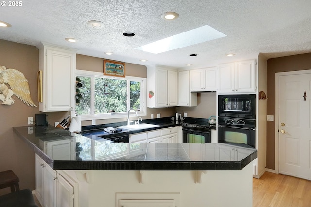 kitchen with a skylight, a sink, black appliances, a peninsula, and a kitchen breakfast bar