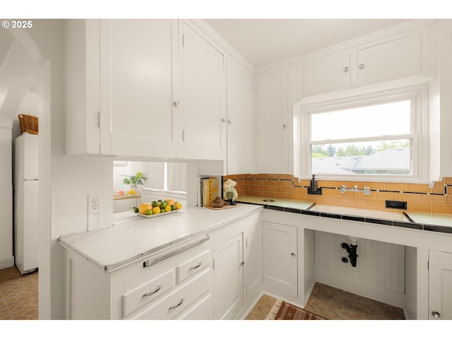 kitchen with freestanding refrigerator, white cabinetry, light tile patterned floors, and backsplash