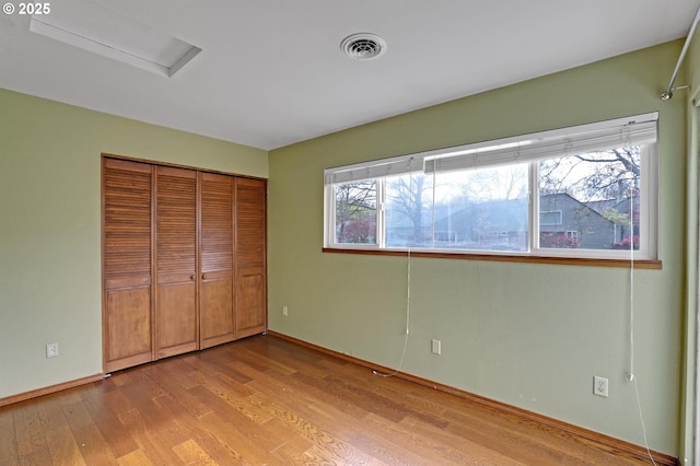 unfurnished bedroom with a closet, visible vents, wood finished floors, attic access, and baseboards