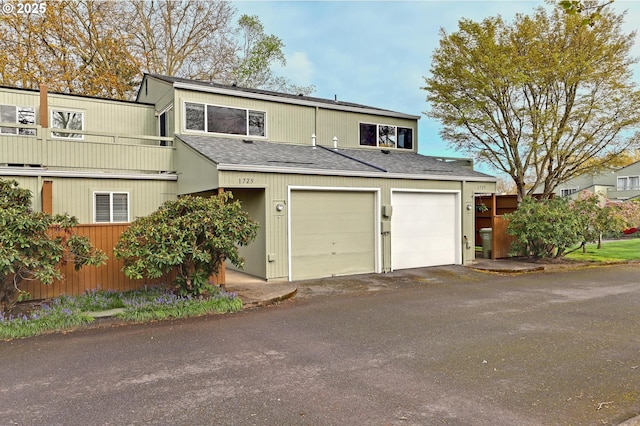 view of front facade with a garage, roof with shingles, a balcony, and driveway