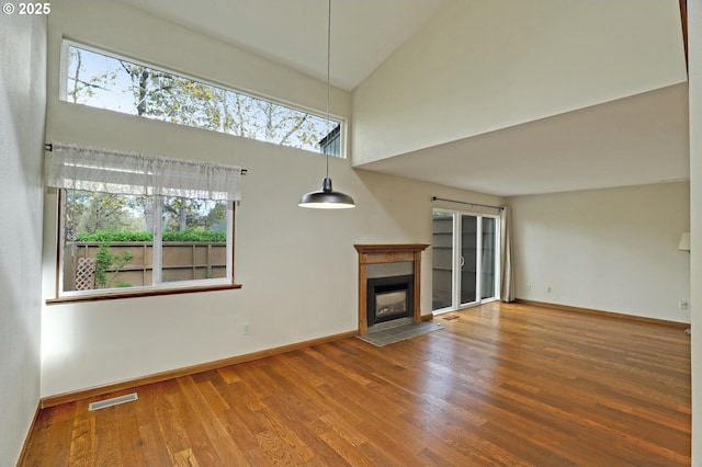 unfurnished living room featuring visible vents, baseboards, a high ceiling, wood finished floors, and a fireplace with flush hearth