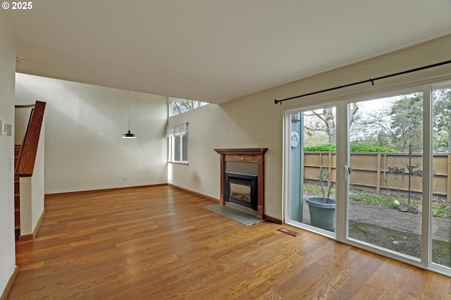 unfurnished living room featuring a healthy amount of sunlight, a fireplace with flush hearth, baseboards, and wood finished floors