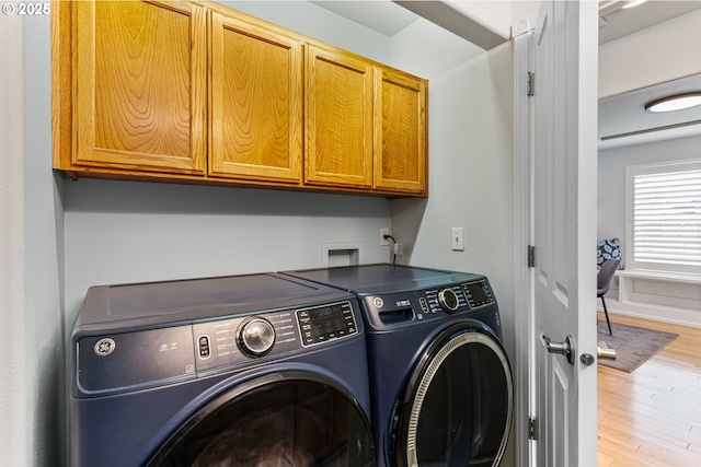 laundry room featuring cabinets, washer and clothes dryer, and light hardwood / wood-style flooring