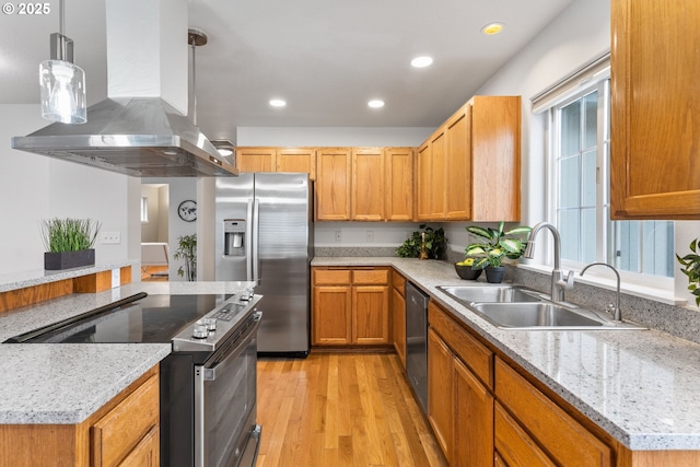 kitchen featuring sink, light stone counters, island range hood, decorative light fixtures, and appliances with stainless steel finishes