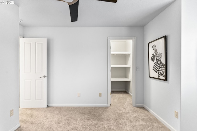 unfurnished bedroom featuring a spacious closet, light colored carpet, a closet, and ceiling fan