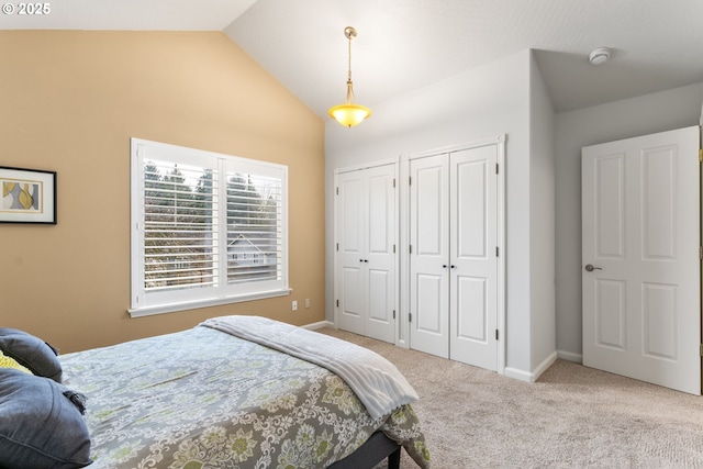 carpeted bedroom featuring multiple closets and vaulted ceiling