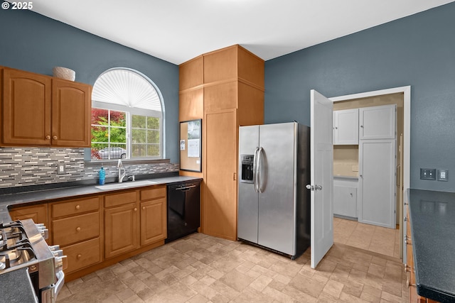 kitchen with appliances with stainless steel finishes, a sink, backsplash, stone finish flooring, and dark countertops