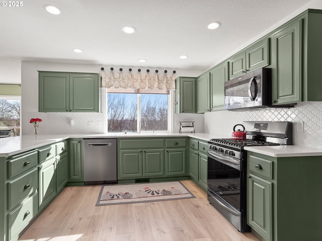 kitchen with a sink, light wood-style floors, stainless steel appliances, and green cabinetry