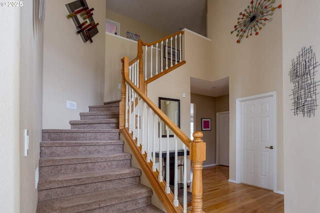 stairs with hardwood / wood-style flooring and a towering ceiling