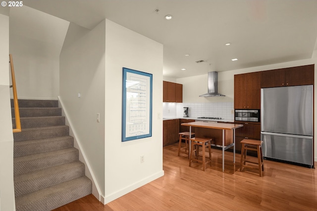 kitchen featuring appliances with stainless steel finishes, tasteful backsplash, a breakfast bar area, a center island, and wall chimney range hood