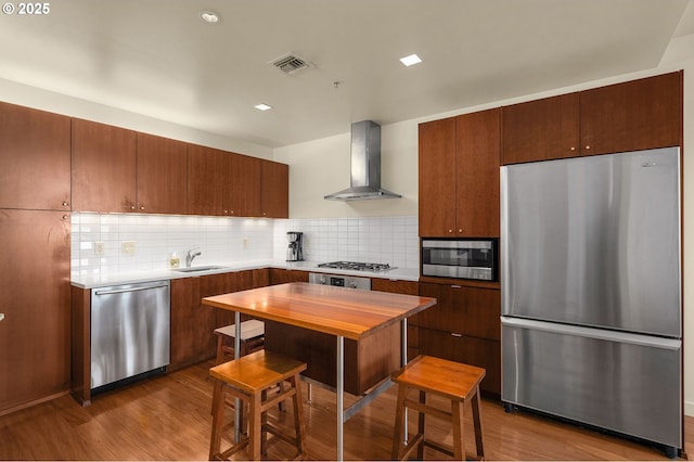 kitchen with tasteful backsplash, light hardwood / wood-style flooring, stainless steel appliances, and wall chimney exhaust hood