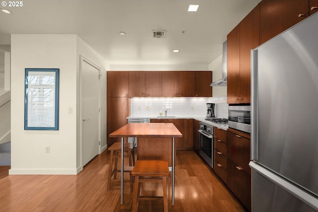 kitchen with a breakfast bar, a center island, light wood-type flooring, appliances with stainless steel finishes, and backsplash