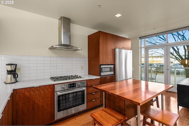 kitchen featuring wall chimney exhaust hood, stainless steel appliances, light hardwood / wood-style flooring, and backsplash