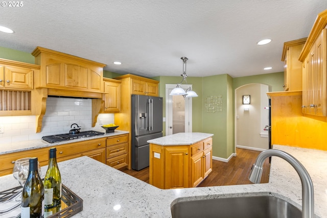 kitchen featuring arched walkways, stainless steel appliances, backsplash, a sink, and light stone countertops