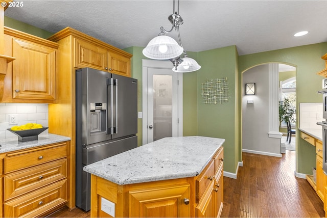 kitchen featuring decorative backsplash, arched walkways, light stone counters, and stainless steel fridge with ice dispenser