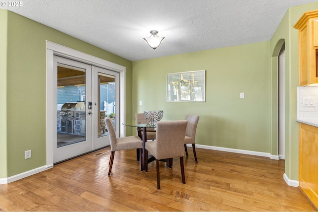 dining area with light wood-style floors, french doors, a textured ceiling, and baseboards