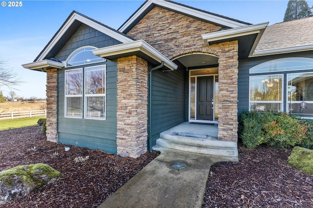 entrance to property featuring stone siding, a shingled roof, and fence