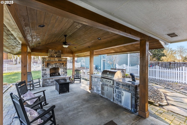 view of patio / terrace with exterior kitchen, an outdoor stone fireplace, a grill, and fence