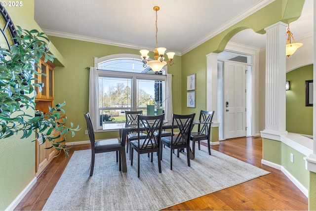 dining space featuring ornate columns, arched walkways, a chandelier, and wood finished floors