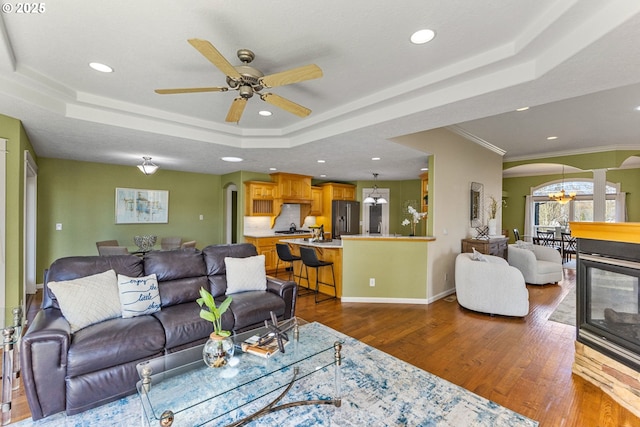 living room featuring dark wood-style floors, a tray ceiling, arched walkways, recessed lighting, and baseboards