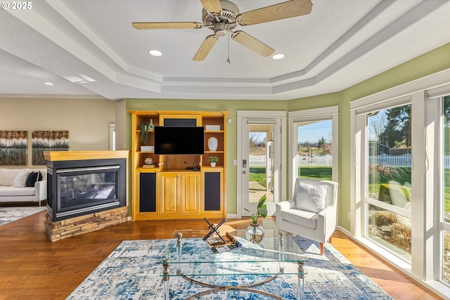 living area with a tray ceiling, recessed lighting, wood finished floors, and a multi sided fireplace