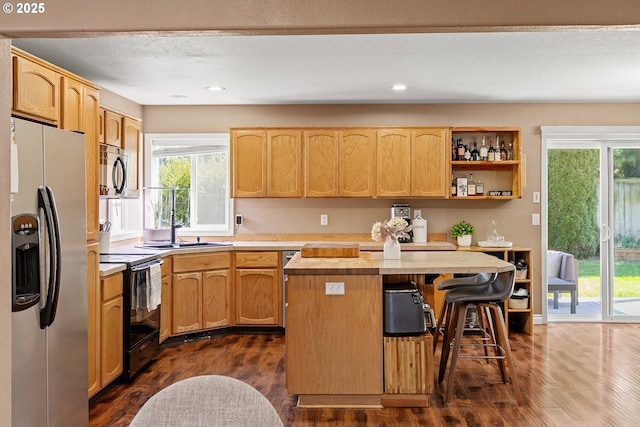 kitchen with light countertops, a kitchen bar, dark wood-style floors, stainless steel appliances, and a kitchen island