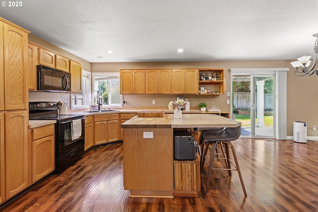 kitchen featuring dark wood-style flooring, a sink, black appliances, a kitchen island, and a breakfast bar area