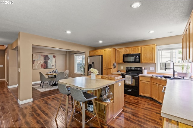 kitchen with a sink, light countertops, black appliances, and dark wood finished floors