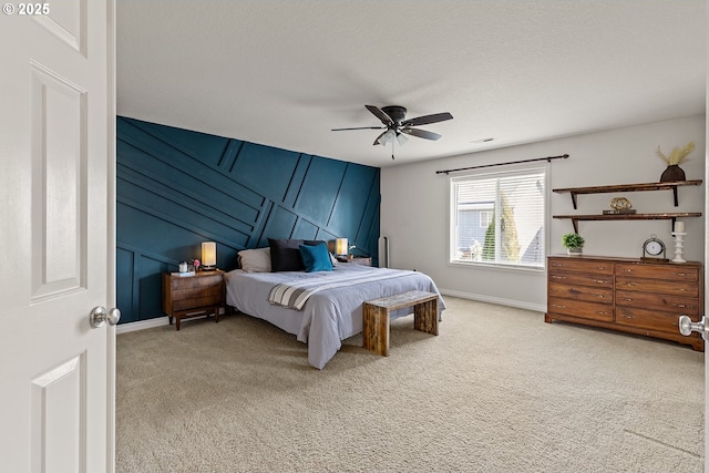 bedroom with a decorative wall, light colored carpet, baseboards, and ceiling fan