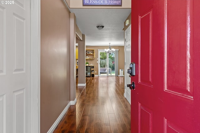 foyer entrance with wood-type flooring, baseboards, a chandelier, and a textured ceiling