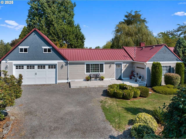 shingle-style home featuring driveway, a patio, metal roof, an attached garage, and a front lawn