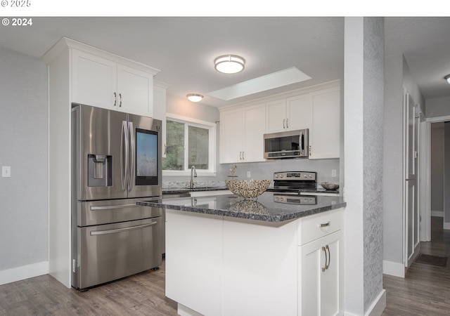 kitchen featuring a center island, white cabinetry, stainless steel appliances, dark stone countertops, and hardwood / wood-style flooring