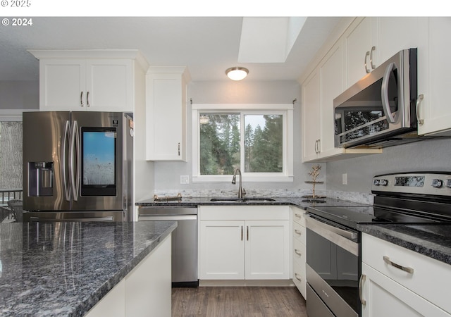 kitchen with white cabinetry, stainless steel appliances, dark stone counters, sink, and dark hardwood / wood-style floors