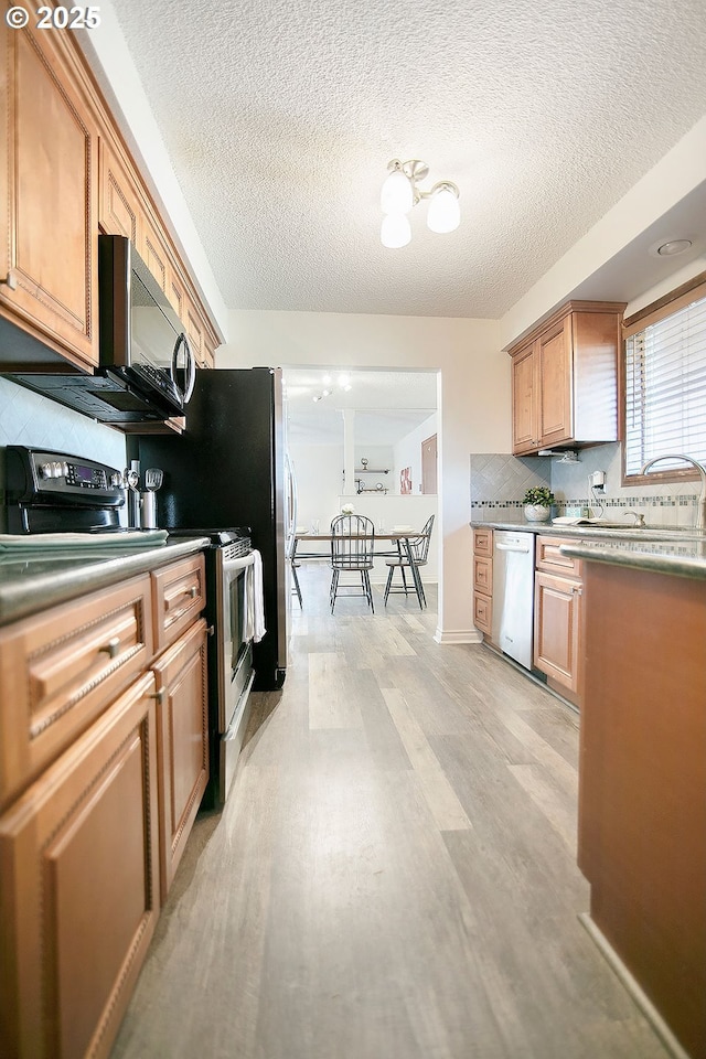 kitchen featuring decorative backsplash, appliances with stainless steel finishes, a sink, a textured ceiling, and light wood-type flooring